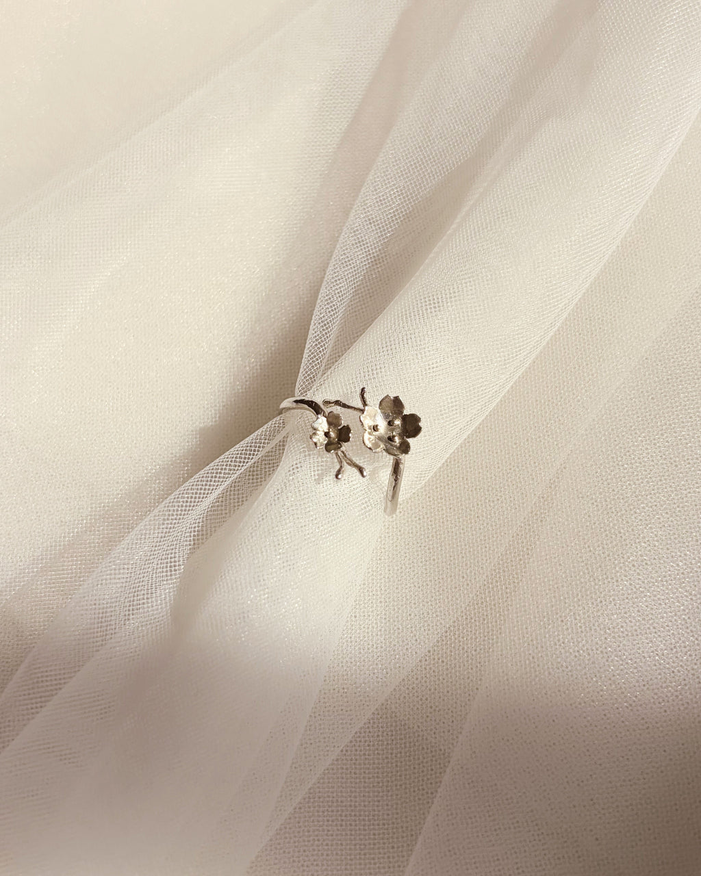 A delicate silver ring with small floral details, resting on soft, draped white tulle fabric.