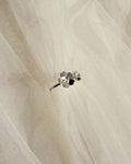 A close-up of a delicate silver-toned ring with small dainty florals set against a soft, sheer white fabric background.