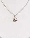 A delicate silver chain necklace with a small circular floral pendant displayed on a white jewelry bust against a neutral indoor background.