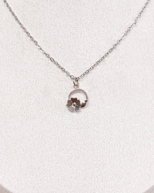 A delicate silver chain necklace with a small circular floral pendant displayed on a white jewelry bust against a neutral indoor background.