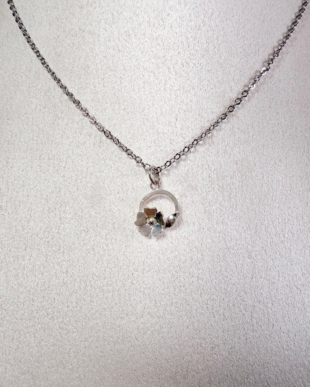 A silver chain necklace with a small circular pendant, displayed on a textured white surface.