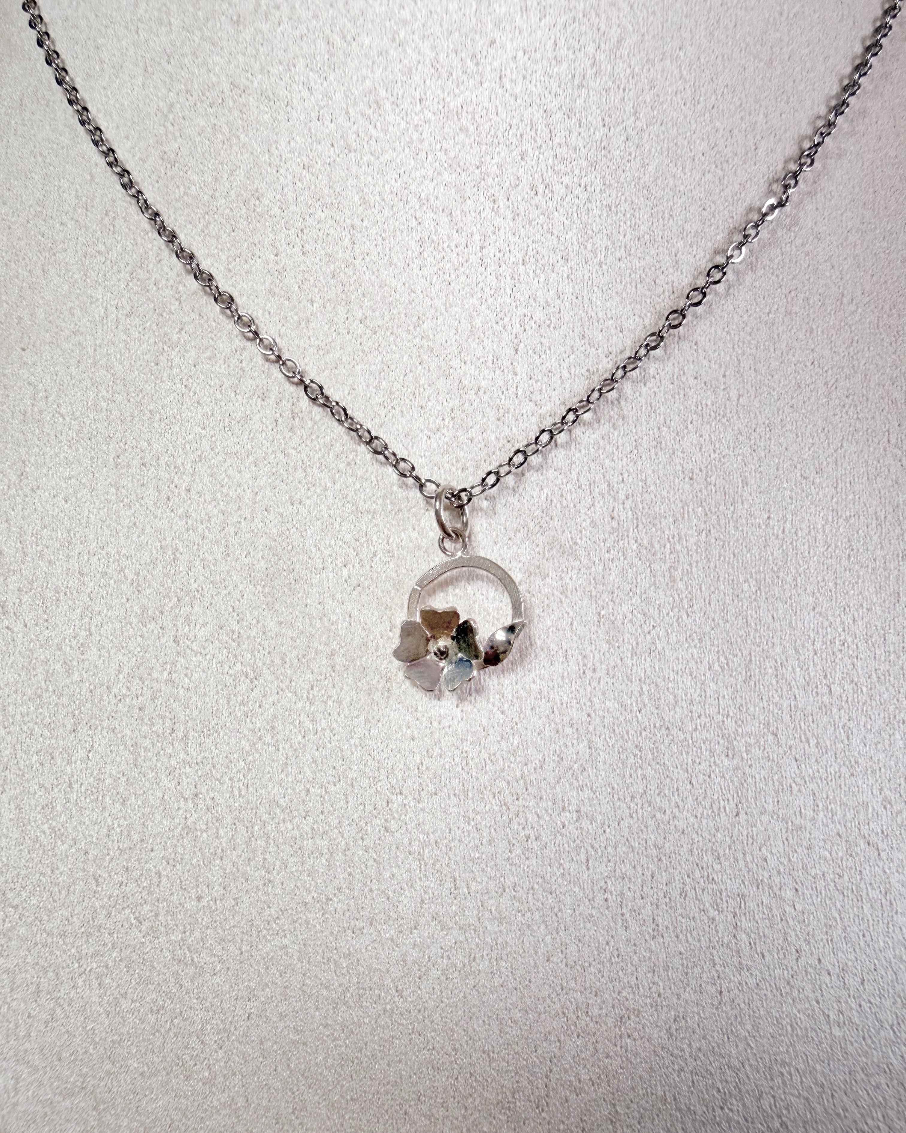 A silver chain necklace with a small circular pendant, displayed on a textured white surface.