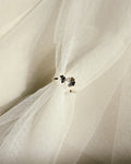 A close-up of a white tulle or mesh fabric with a  silver floral ring near the center, set against draped folds of the same translucent white material.