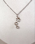 A silver daisy necklace with a delicate chain and three small flower charms, displayed on a white textured jewelry bust.