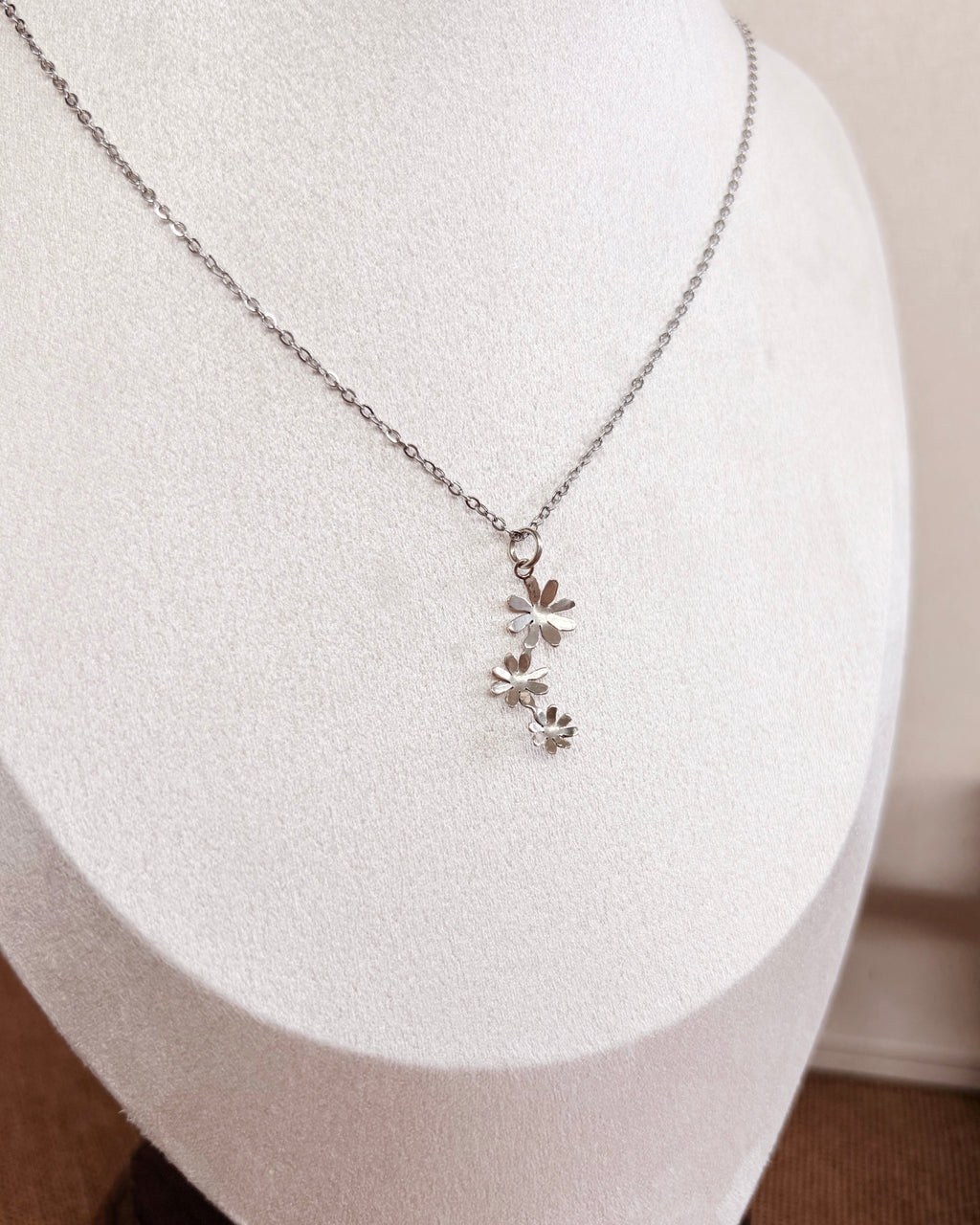 A delicate silver necklace with a small floral cluster pendant, displayed on a white jewelry bust.