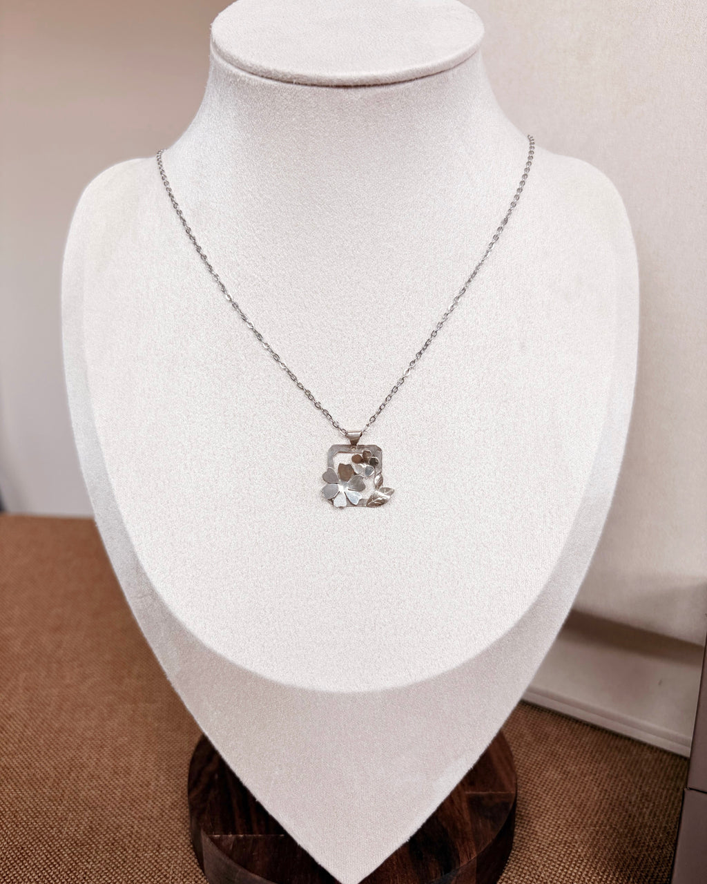 A silver chain necklace with a botanical pendant displayed on a white jewelry bust.