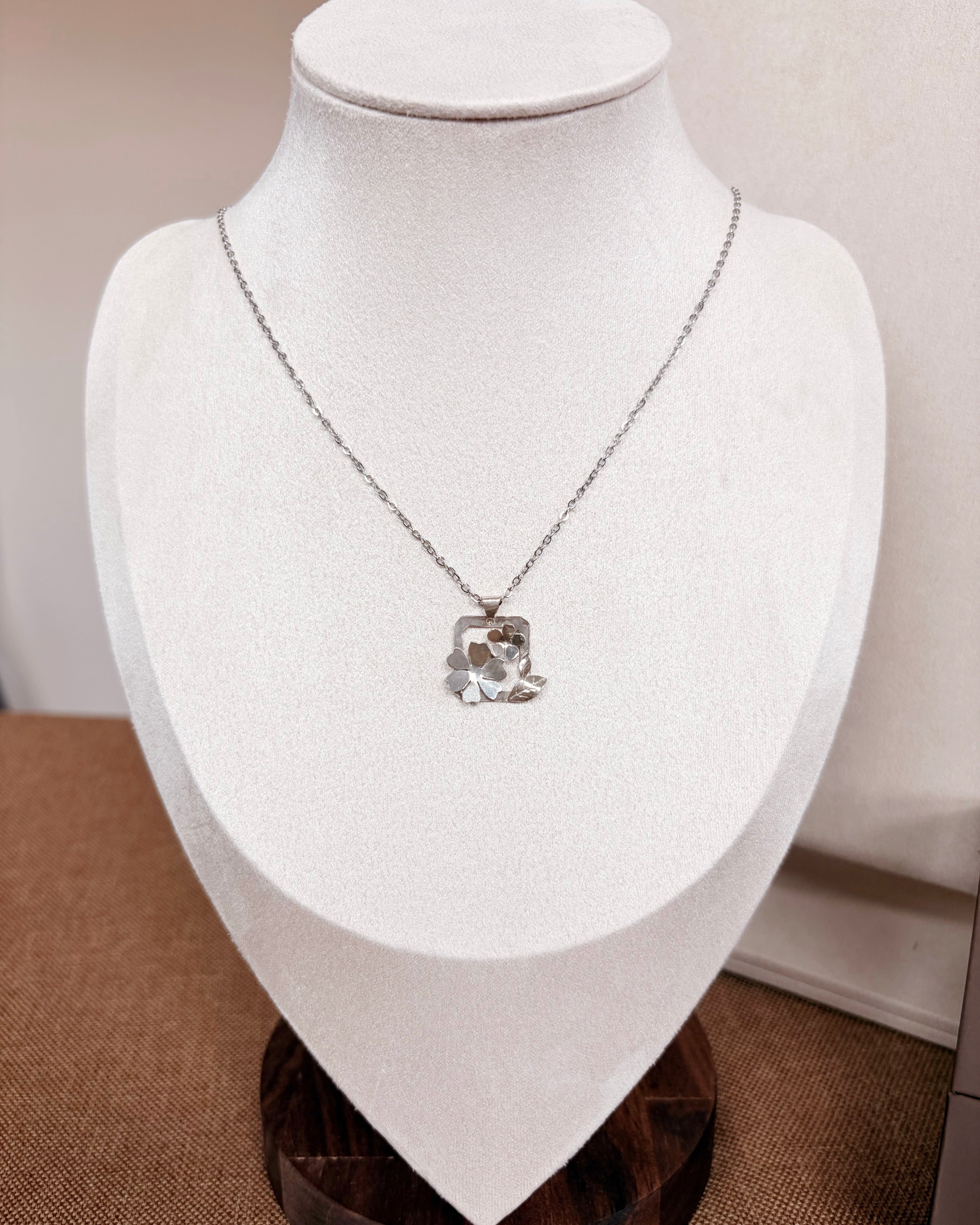 A silver chain necklace with a botanical pendant displayed on a white jewelry bust.