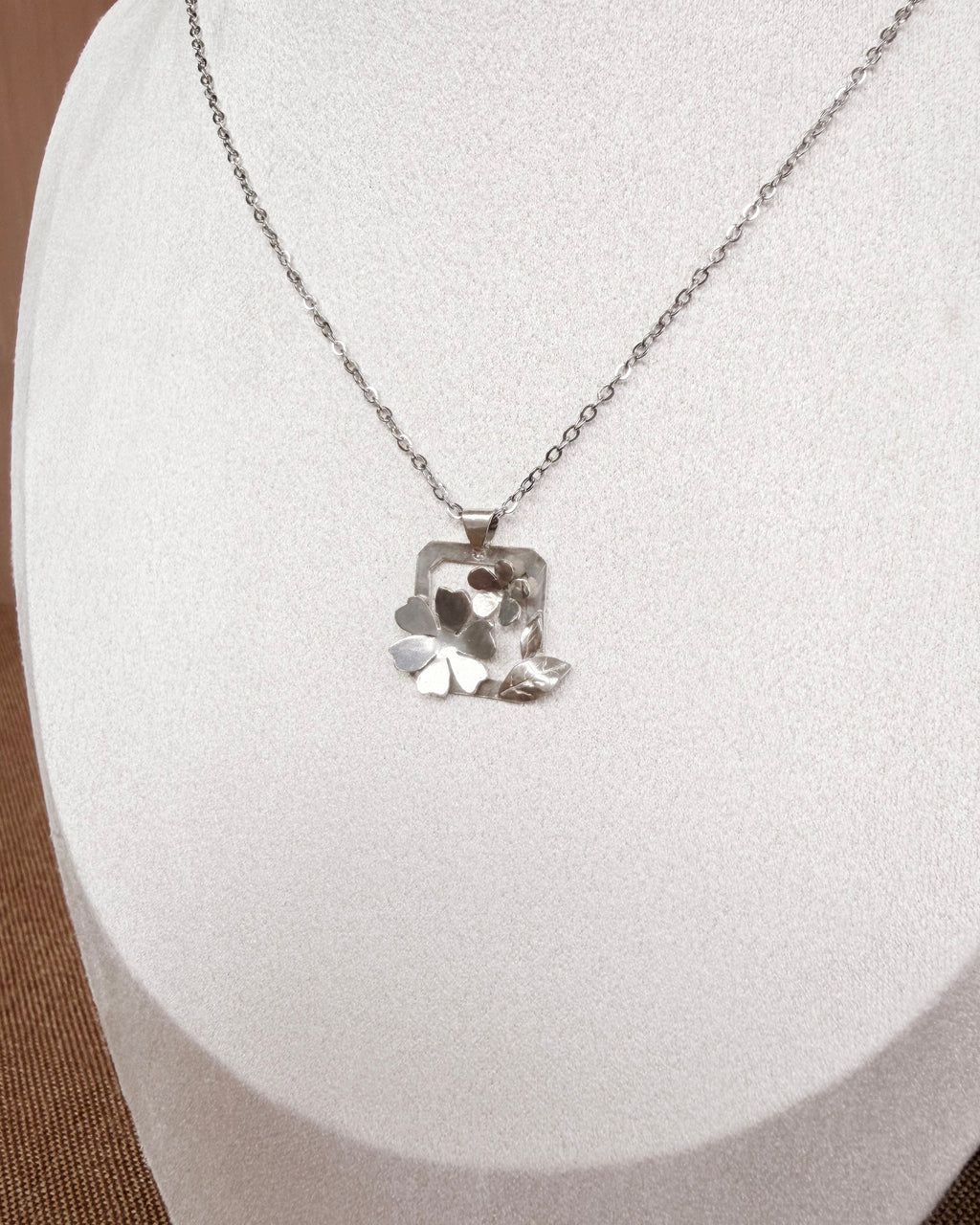 A silver-toned necklace with a textured, organic-shaped pendant displayed on a white jewelry bust.