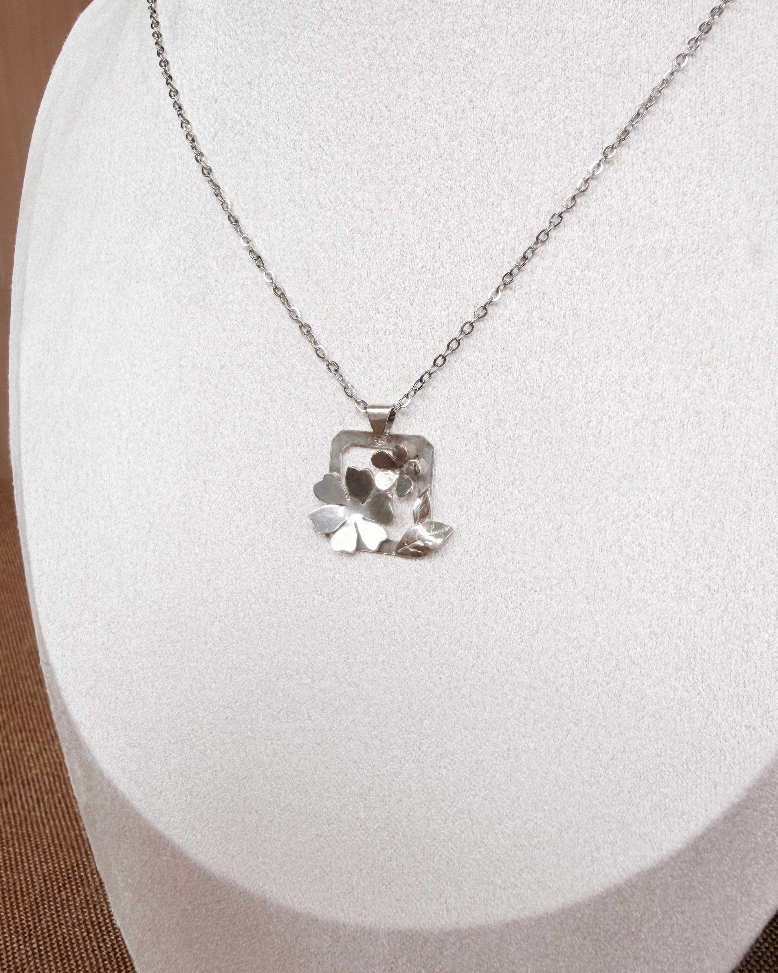 A silver-toned necklace with a textured, organic-shaped pendant displayed on a white jewelry bust.