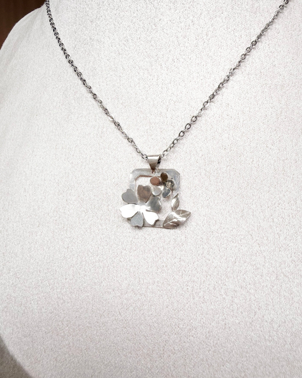 A silver necklace with a textured, organic-shaped pendant displayed on a white fabric jewelry bust.