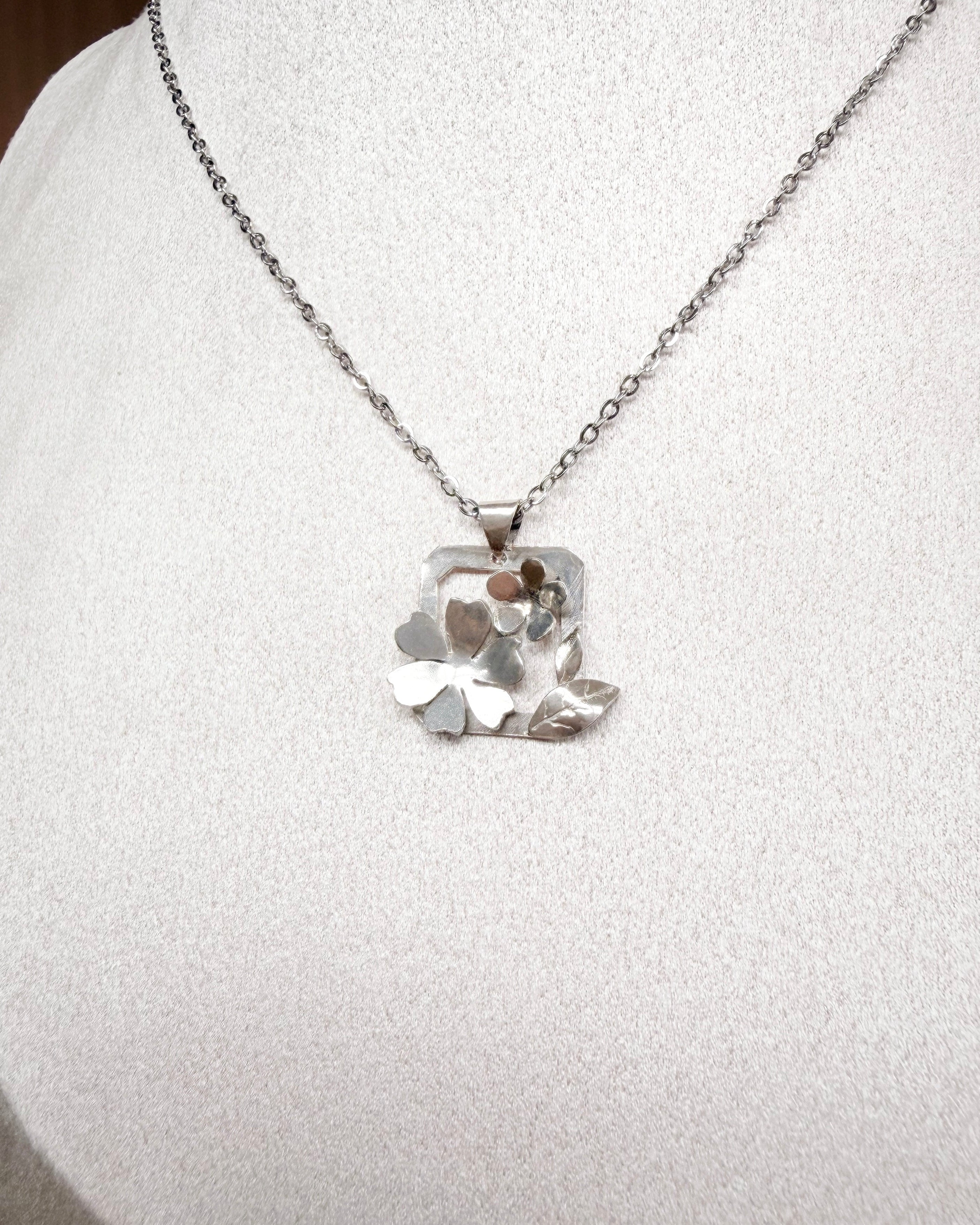 A silver necklace with a textured, organic-shaped pendant displayed on a white fabric jewelry bust.