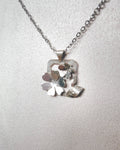 A silver necklace with a geometric floral pendant featuring layered metallic leaves and petals, displayed on a textured light gray bust.