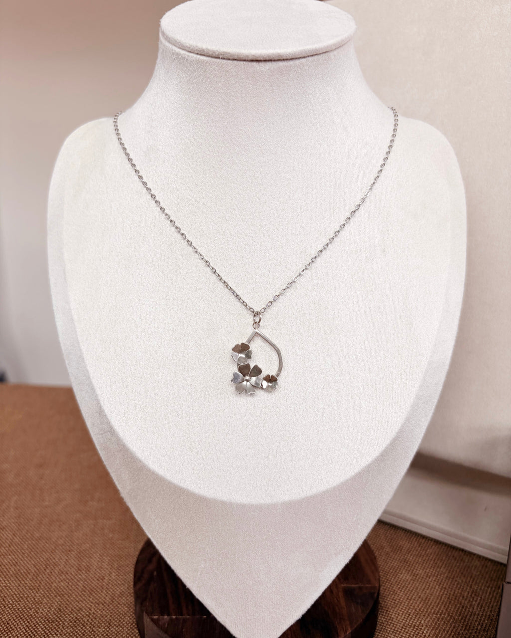 A delicate silver necklace with a crescent moon and small flower pendant, displayed on a white jewelry bust.