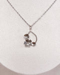 A delicate silver chain necklace with a small floral pendant, displayed on a white fabric jewelry bust.