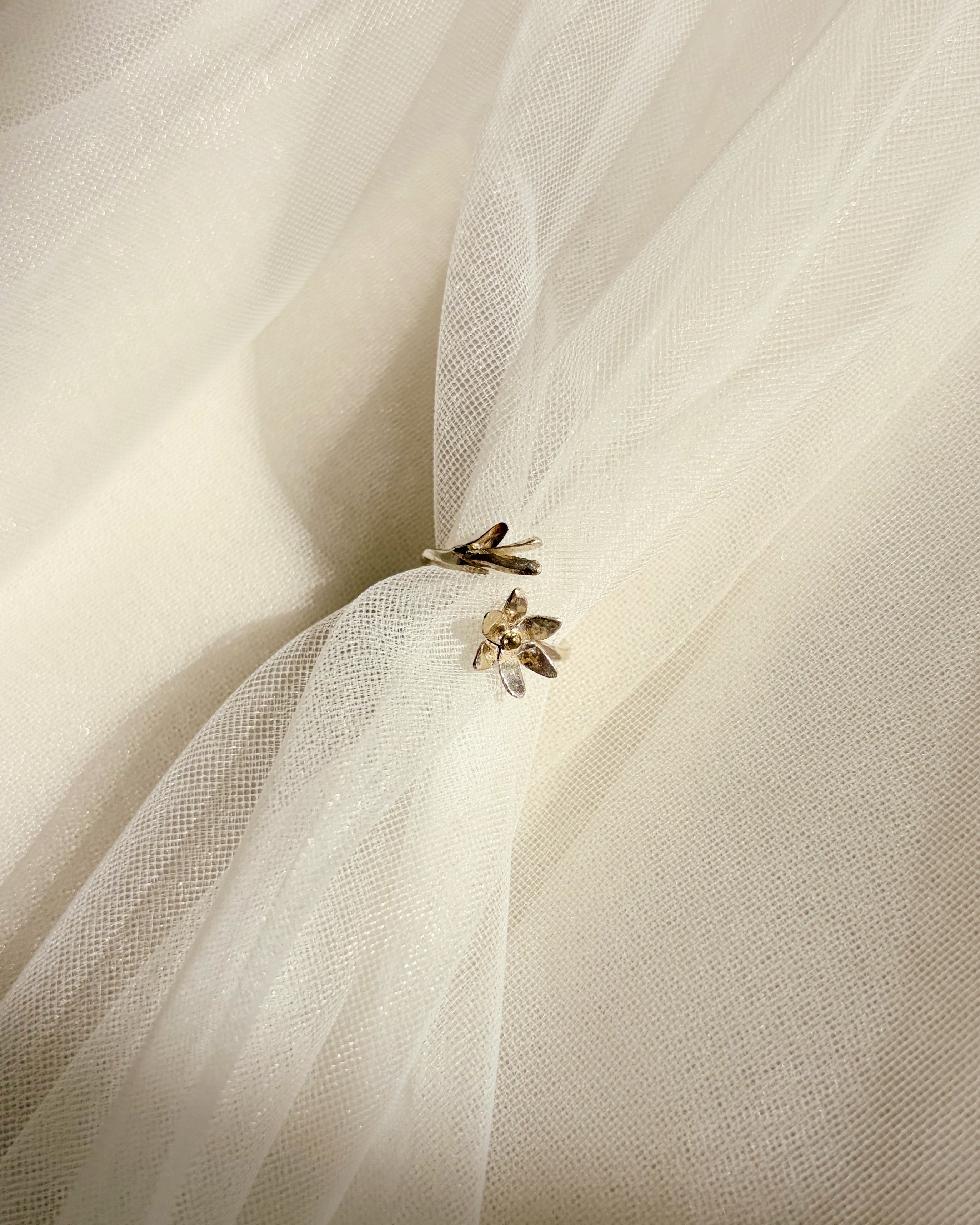 A close-up of a silver floral ring resting on ivory tulle fabric, likely a bridal veil or dress fabric, gathered at a point.