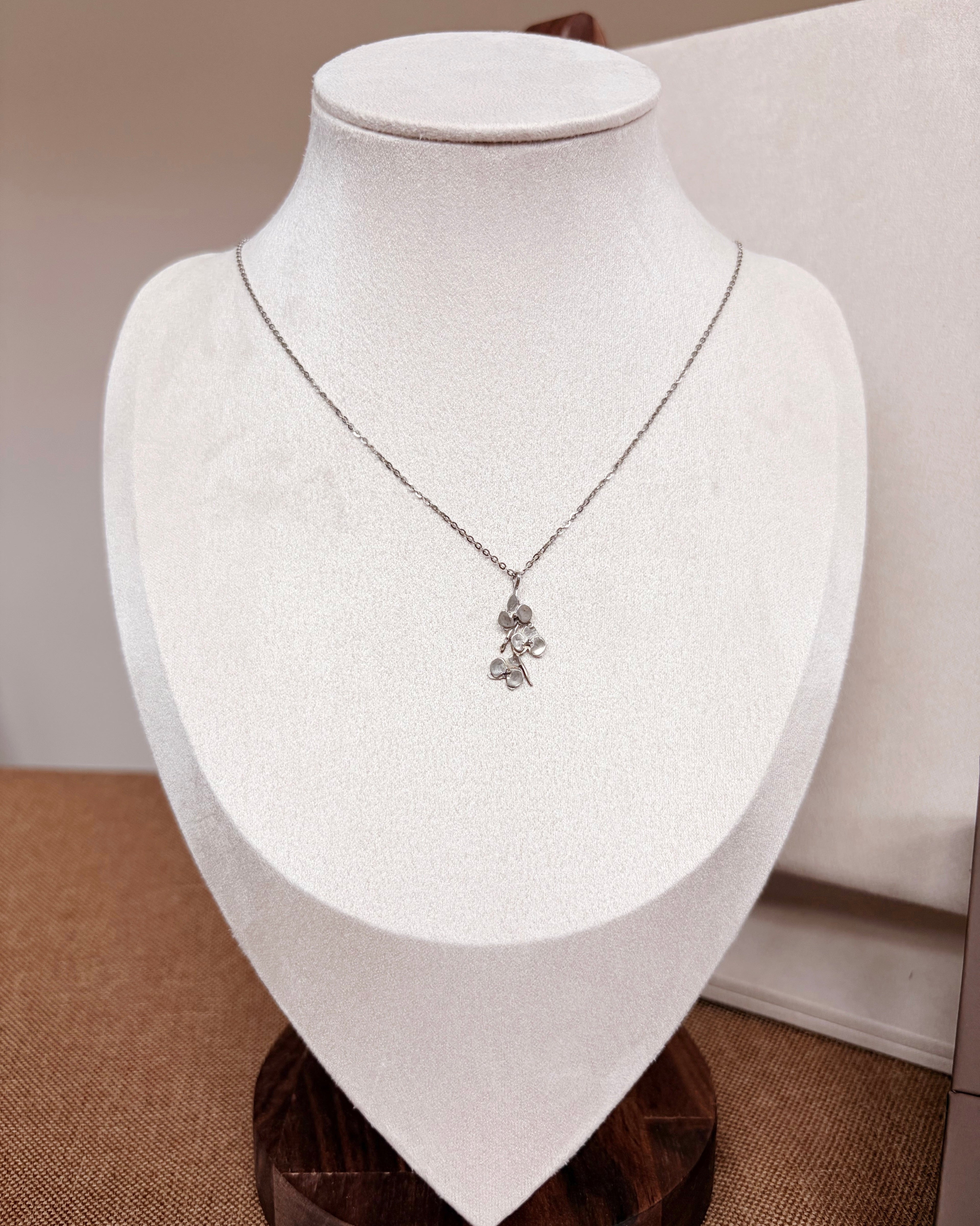 A delicate silver-toned necklace with a small orchid pendant displayed on a white fabric jewelry bust.