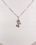 A delicate silver-toned necklace with a small orchid pendant displayed on a white jewelry bust against a warm brown textured background.