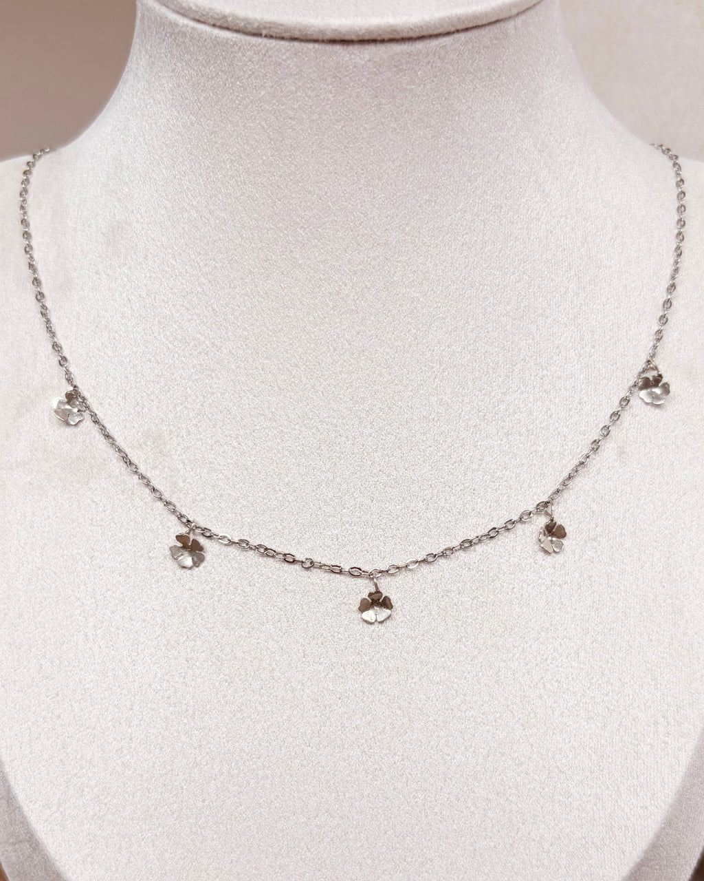 A delicate silver chain necklace with five small floral pendants, displayed on a white jewelry bust.