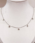A delicate silver chain necklace with five small floral pendants, displayed on a white jewelry bust.