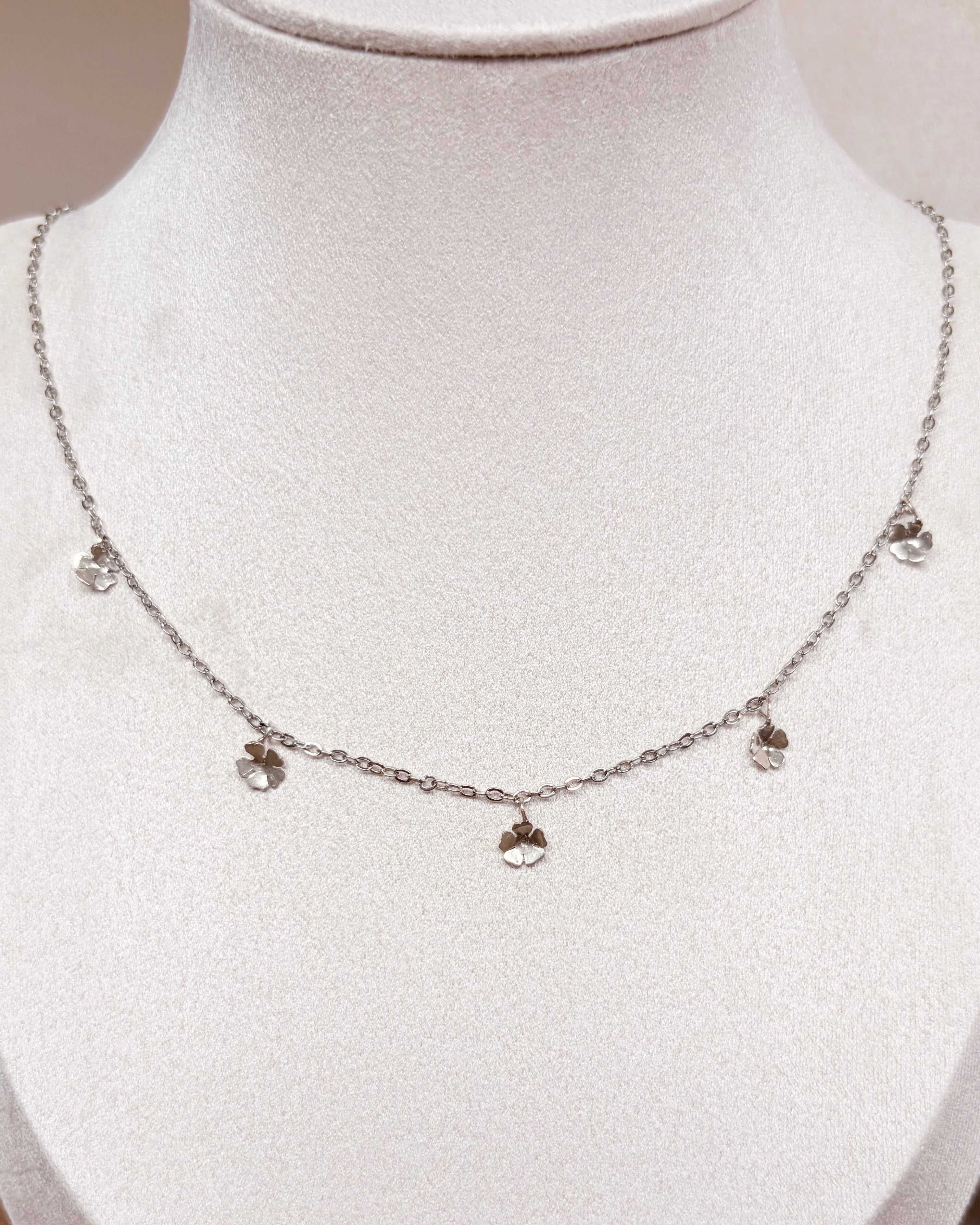 A delicate silver chain necklace with five small floral pendants, displayed on a white jewelry bust.