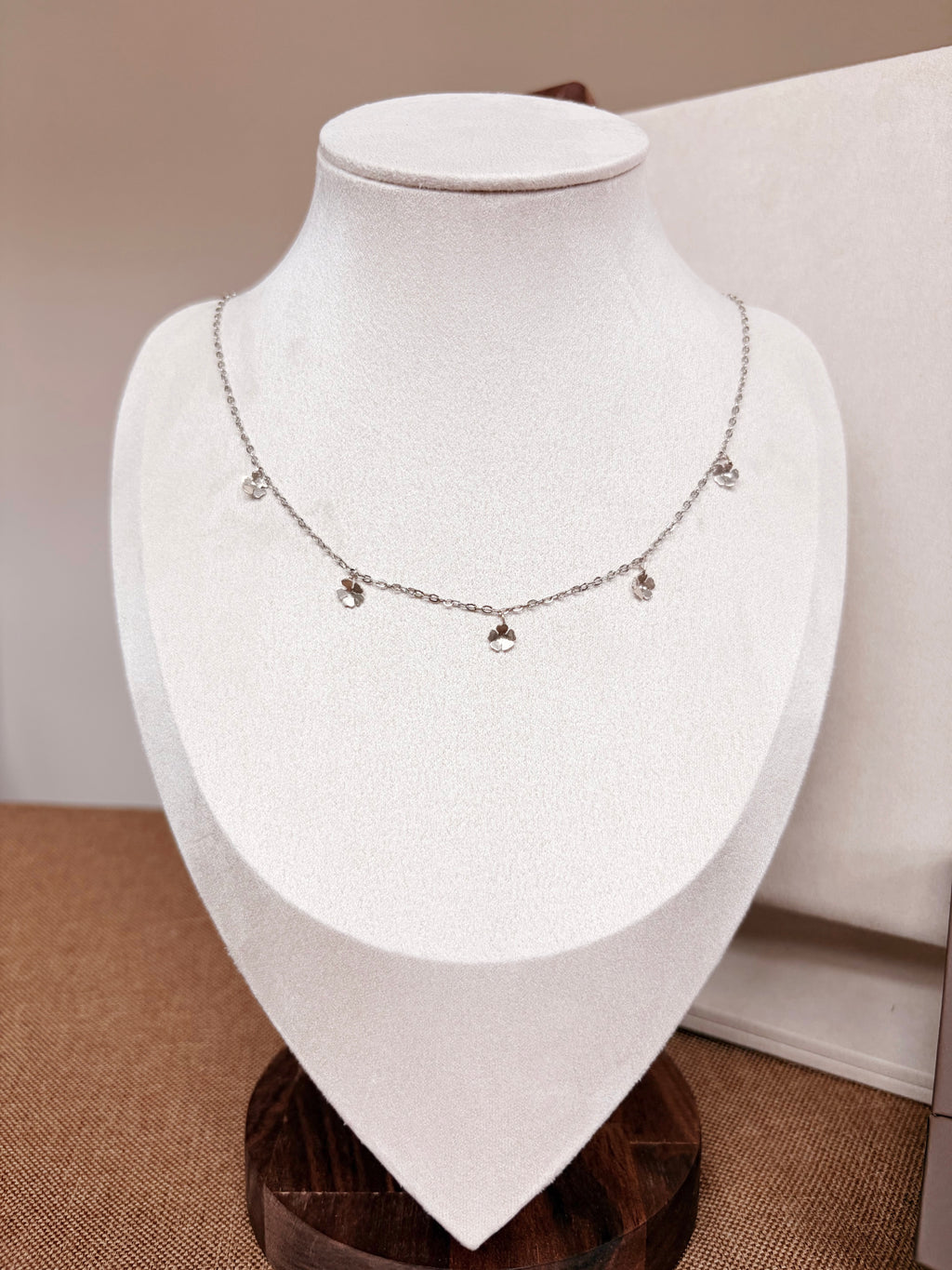 A delicate silver necklace with small dangling charms displayed on a white jewelry bust.