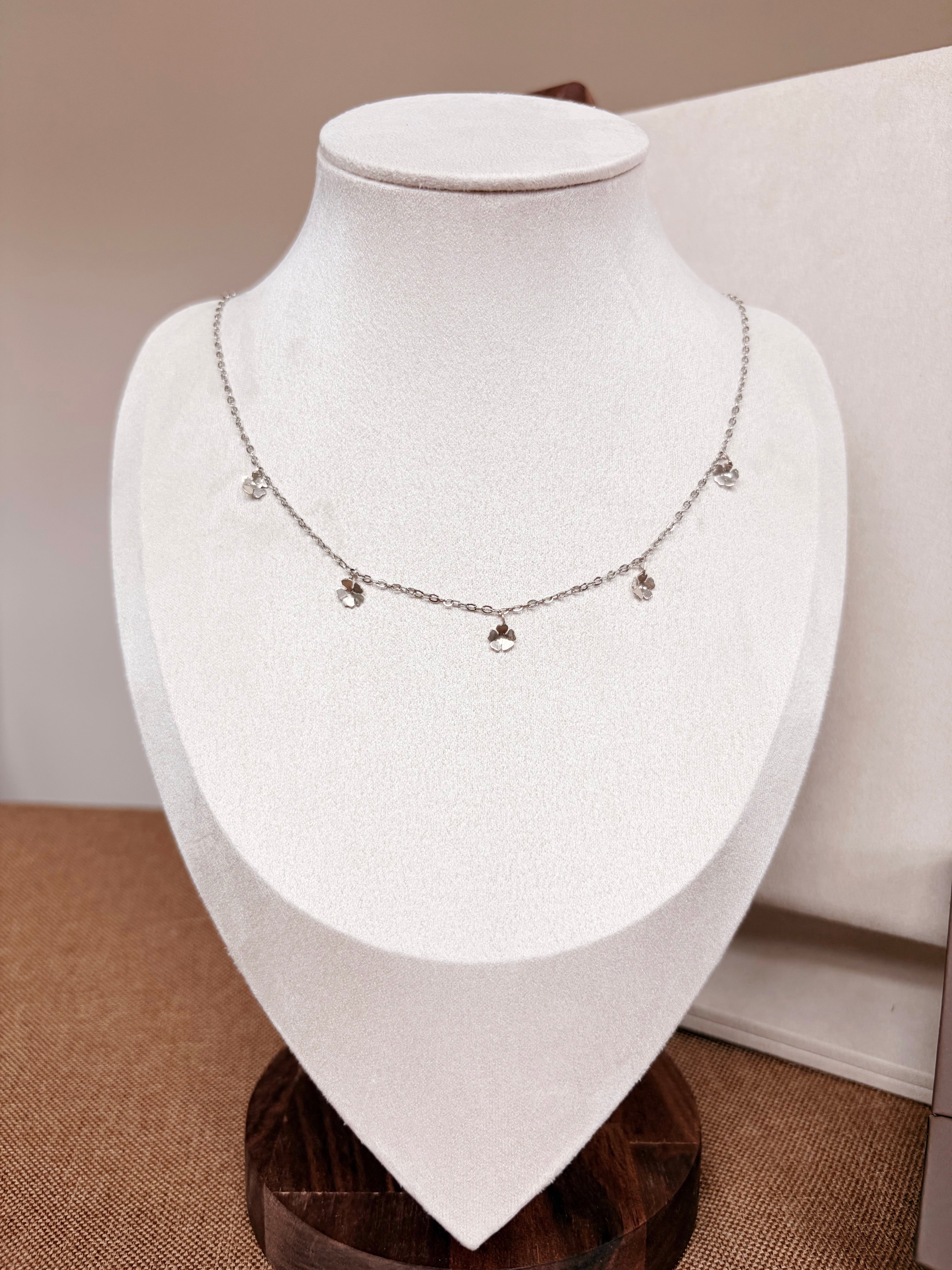 A delicate silver necklace with small dangling charms displayed on a white jewelry bust.