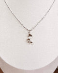 A delicate silver chain necklace with a small silver floral pendant displayed on a white jewelry bust.