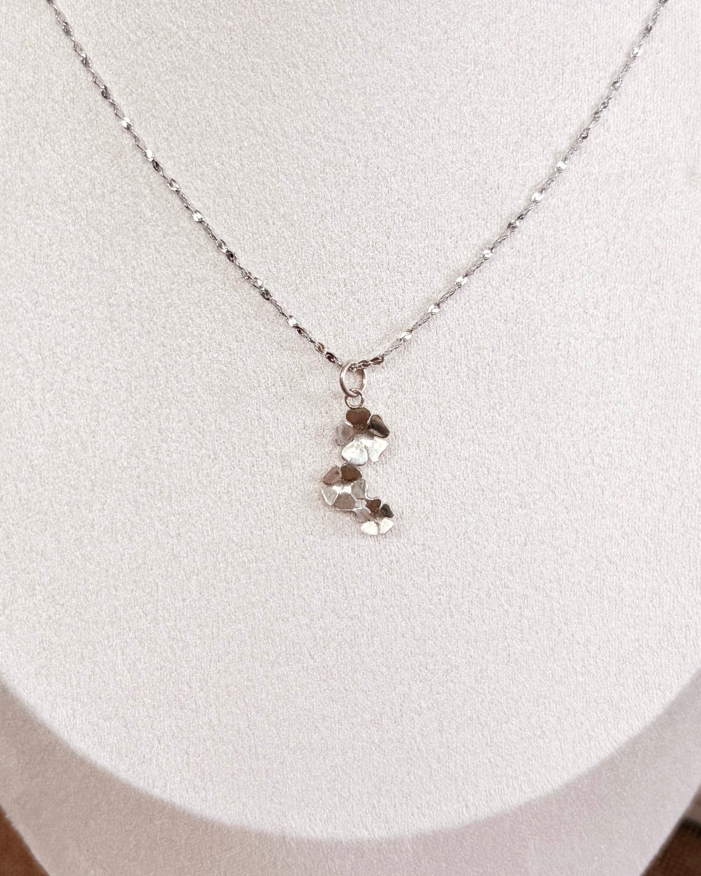 A delicate silver chain necklace with a small silver floral pendant displayed on a white jewelry bust.