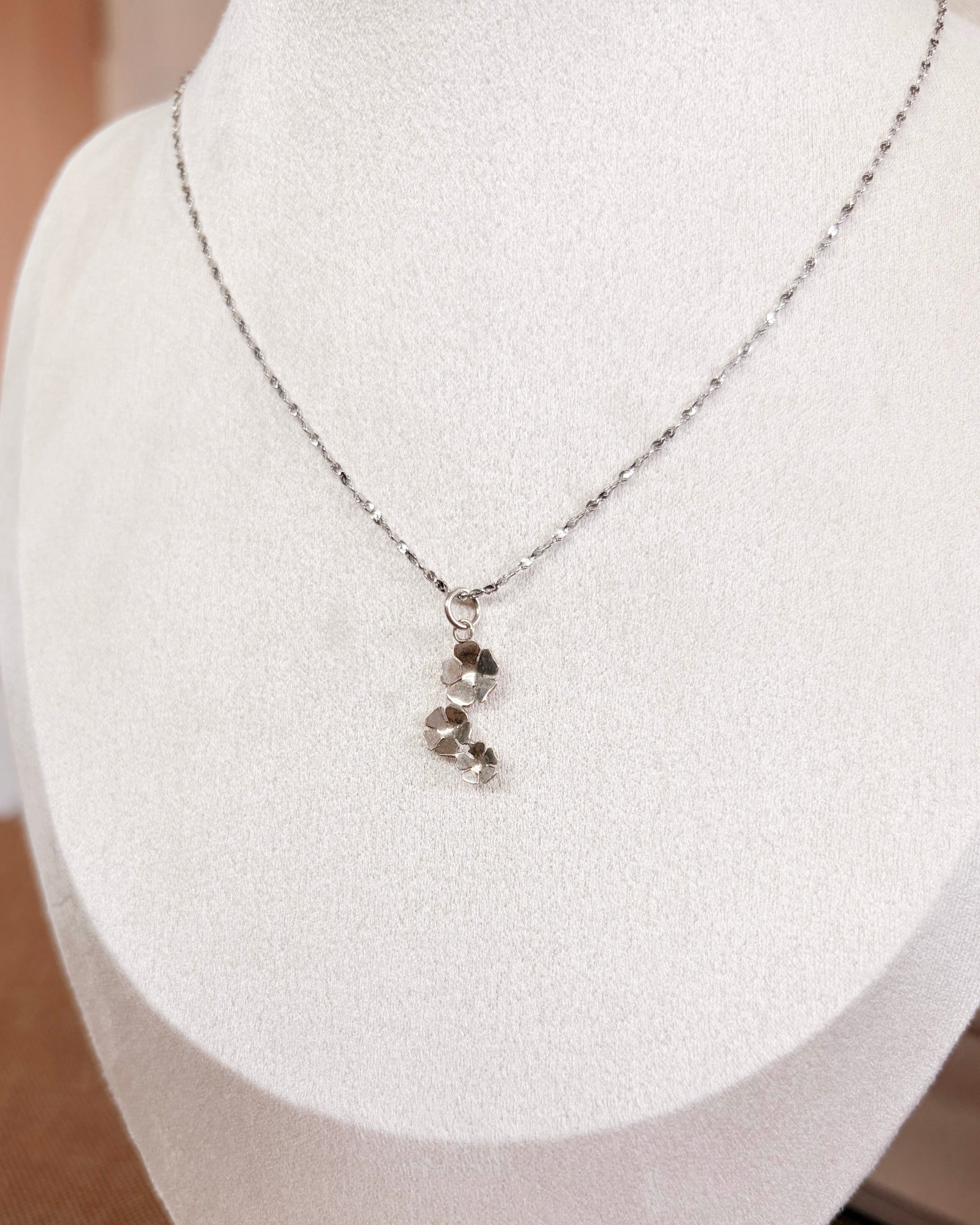 A delicate silver chain necklace with a small cluster of flowers on a white jewelry display bust.