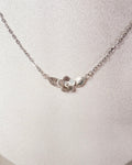 A delicate silver chain necklace with a small textured metal flower pendant, displayed on a textured white jewelry bust.