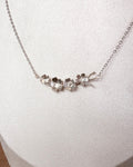 A silver necklace with a delicate chain and a central cluster of small, organic-shaped silver flower charms, displayed on a textured white jewelry bust.