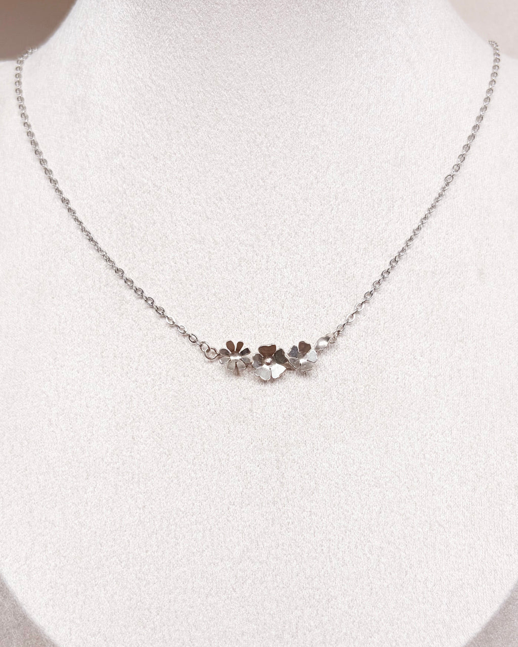 A delicate silver chain necklace with a small floral cluster pendant, displayed on a white jewelry bust.