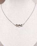 A delicate silver chain necklace with a small floral cluster pendant, displayed on a white jewelry bust.