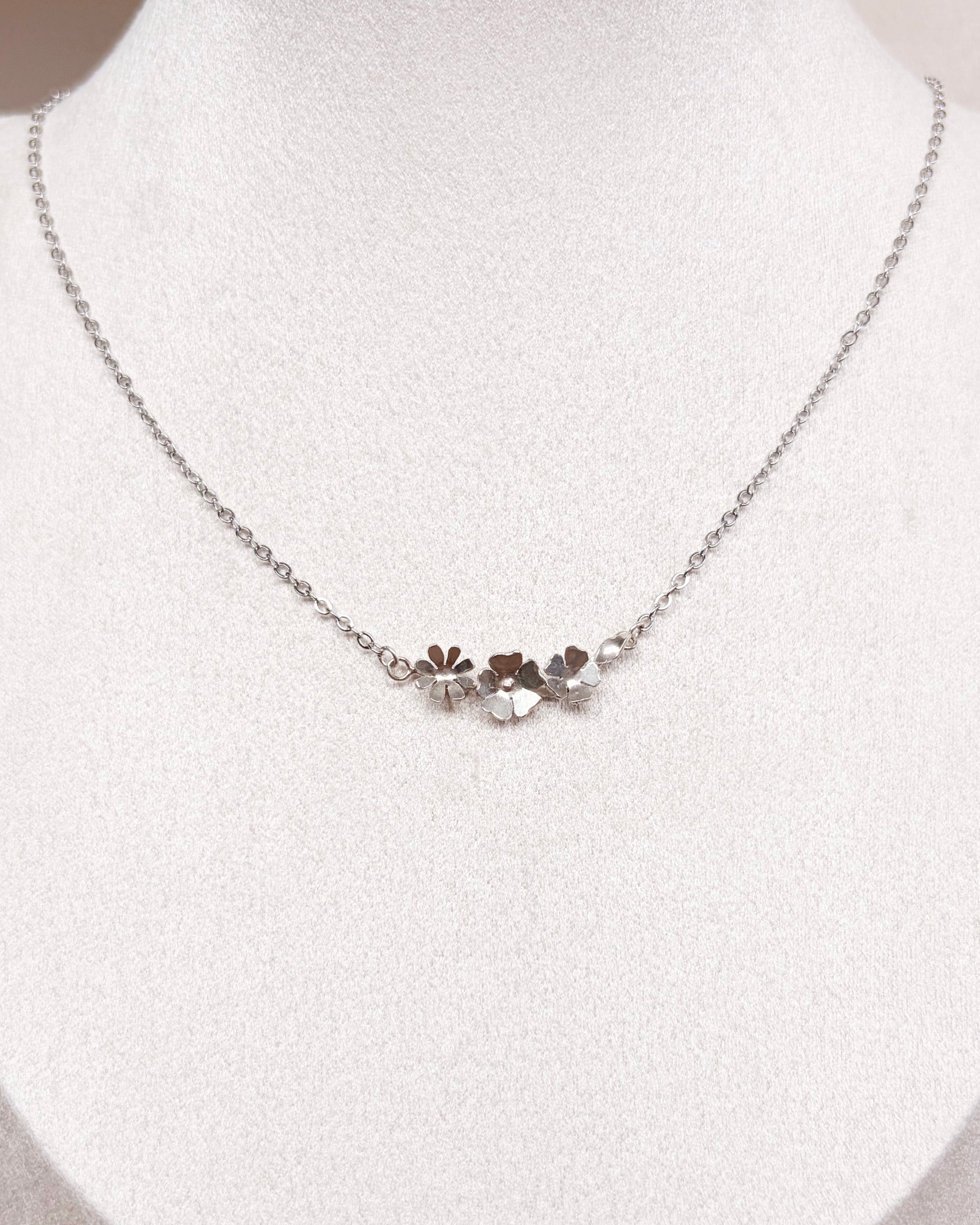 A delicate silver chain necklace with a small floral cluster pendant, displayed on a white jewelry bust.