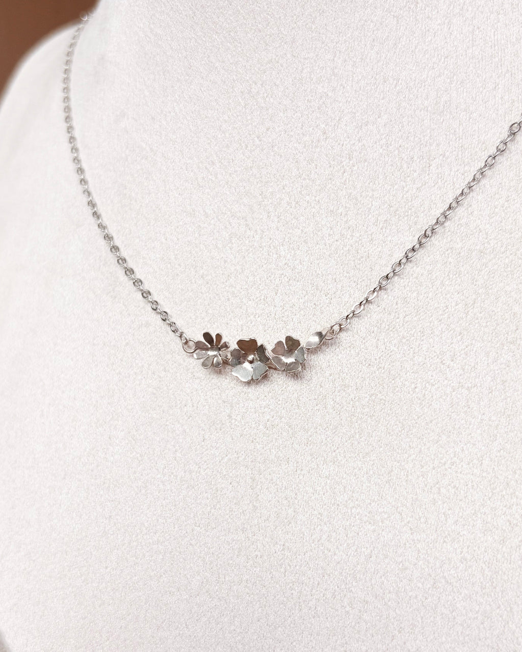 A delicate silver chain necklace with a small central cluster of flowers, displayed on a white jewelry bust.