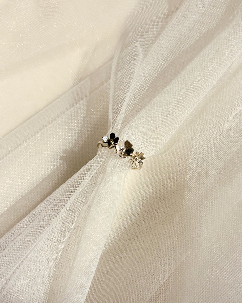 A pair of small silver-toned ring with dainty wildflowers resting on draped white tulle fabric.