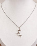 A delicate silver chain necklace with a small cluster of wildflowers pendants displayed on a white fabric jewelry bust.