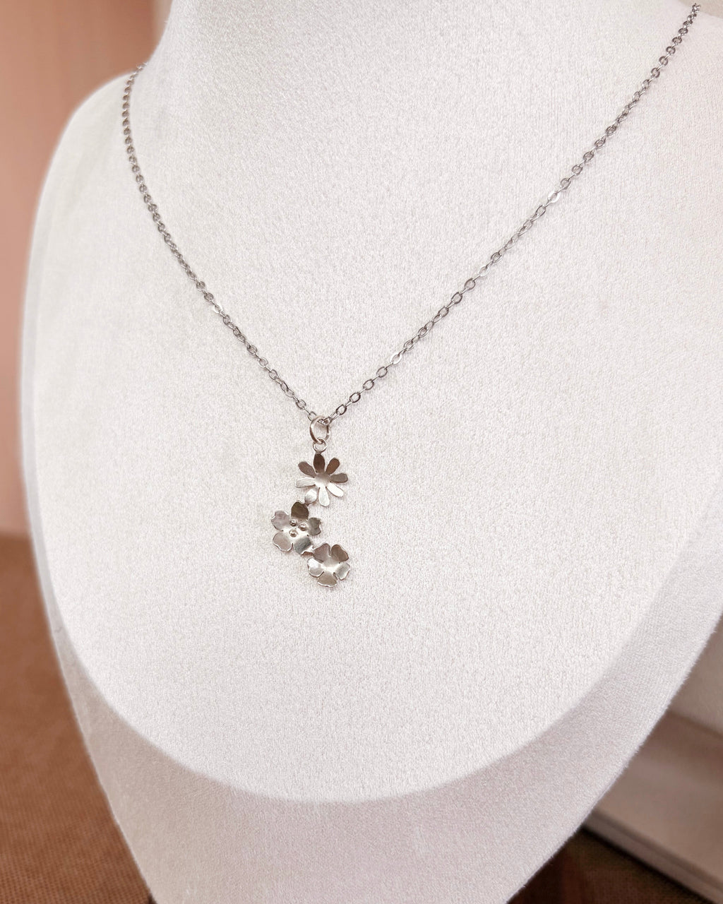 A delicate silver chain necklace with a small floral pendant displayed on a white jewelry bust.